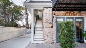 Un escalier menant à une porte, avec un mur en briques, un petit jardin et un toit en métal.