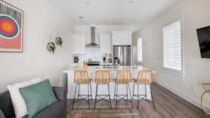 A modern kitchen with white cabinets, a stainless steel refrigerator, and a central island with bar stools. - Urban Sol | Newly Built in Downtown Charleston! (Charleston)