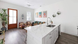 A modern kitchen with a white marble island, wooden flooring, and a built-in sink. - Urban Sol | Newly Built in Downtown Charleston! (Charleston)
