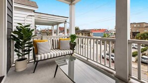 A covered balcony with a glass table and striped sofa, potted plants, and a view of the street and buildings. - Urban Sol | Newly Built in Downtown Charleston! (Charleston)
