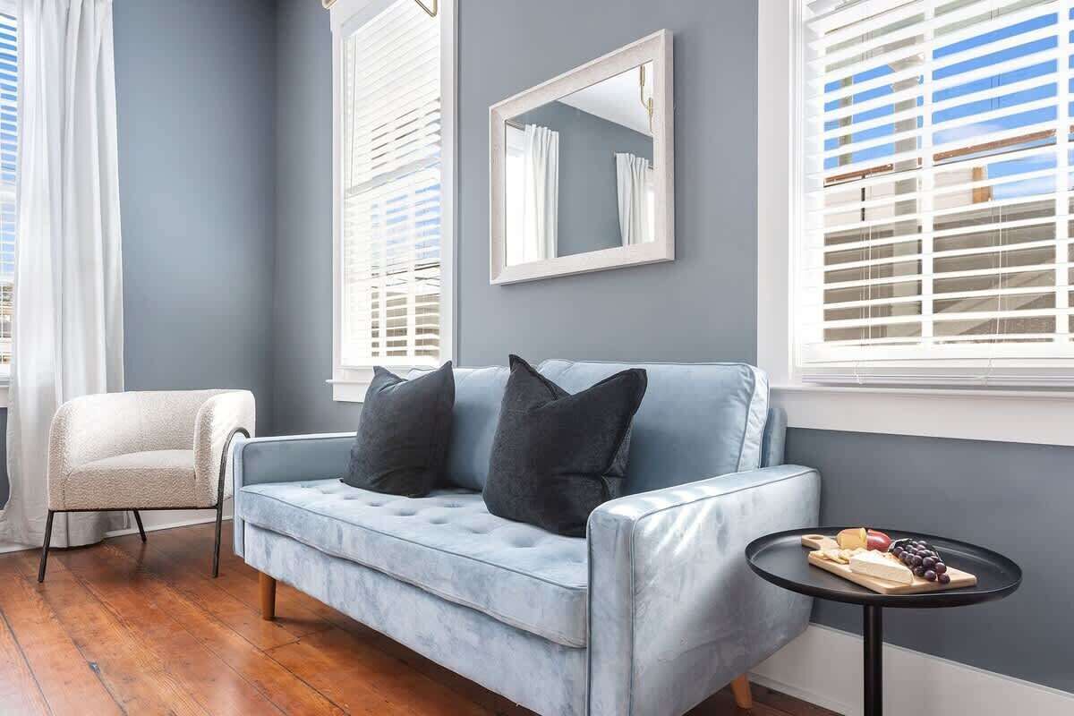 A room with a light blue sofa, a small round table with a cheese board, and a chair.