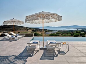 A poolside area with lounge chairs and umbrellas, overlooking a scenic landscape with hills and a body of water.