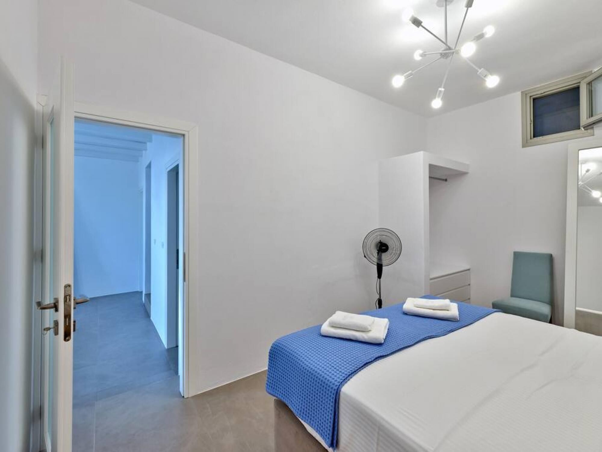 Une chambre d’hôtel avec un lit, un ventilateur, une chaise et un téléviseur fixé au mur.