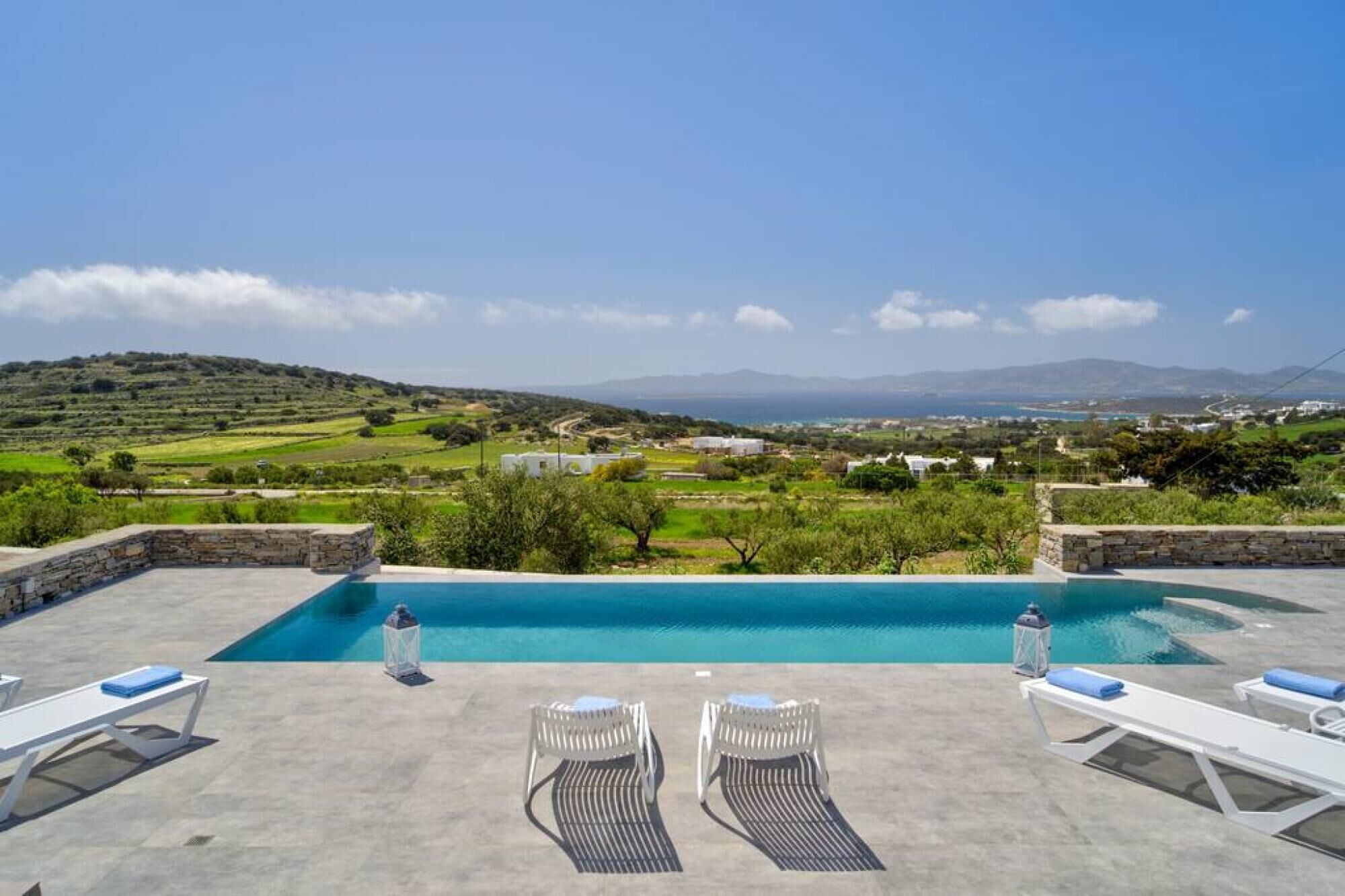 A pool with lounge chairs and a view of a green landscape and mountains.