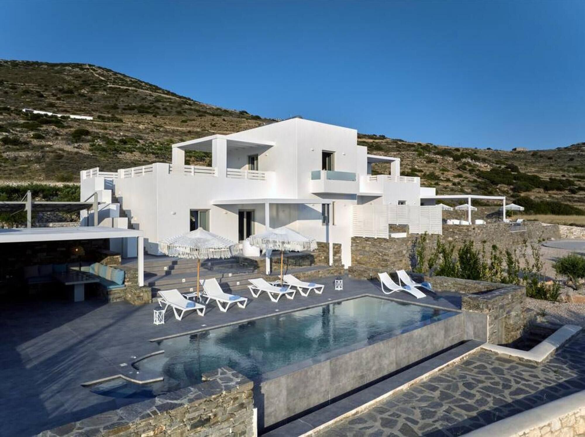 Una villa moderna y blanca con piscina, sillas de descanso y sombrillas.