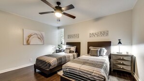 Quarto com duas camas, ventilador de teto, obras de arte e mesa de cabeceira com abajur.