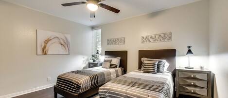 Un dormitorio con dos camas, ventilador de techo, obras de arte y una mesita de noche con lámpara.