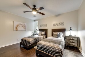 A bedroom with two beds, a ceiling fan, a nightstand with a lamp, and artwork on the walls.