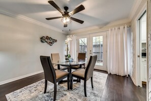 A dining room with a round table, four chairs, a ceiling fan, and a large window with curtains.