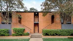 A brick building with a central entrance, a small balcony, and a covered stairway.