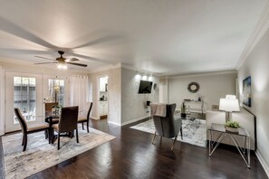 A spacious living area with a dining table, chairs, a sofa, and a TV mounted on the wall. - GP66B - |G. Prairie Escape |2BD | Pool | Workspace (Grand Prairie)