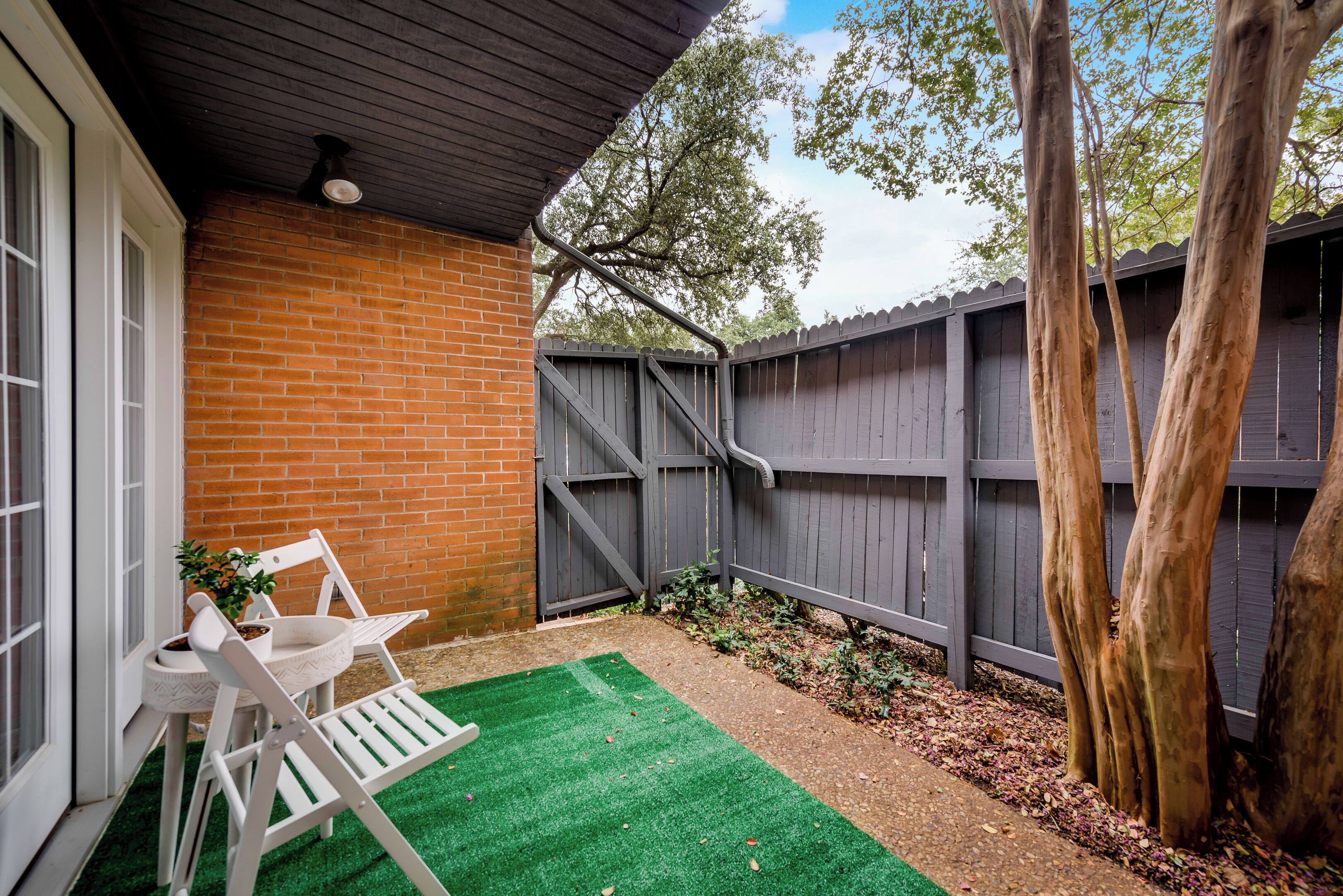 Un patio con pared de ladrillo, cerca de madera y una silla blanca.