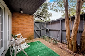 Un patio con pared de ladrillo, cerca de madera y una silla blanca.