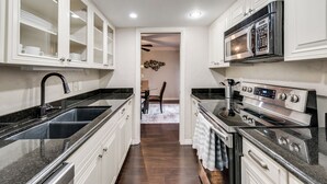A narrow kitchen with white cabinetry, a stainless steel sink, a microwave, and an oven. - GP66B - Stylish 2BD Condo | Pool | Grand Prairie (Grand Prairie)