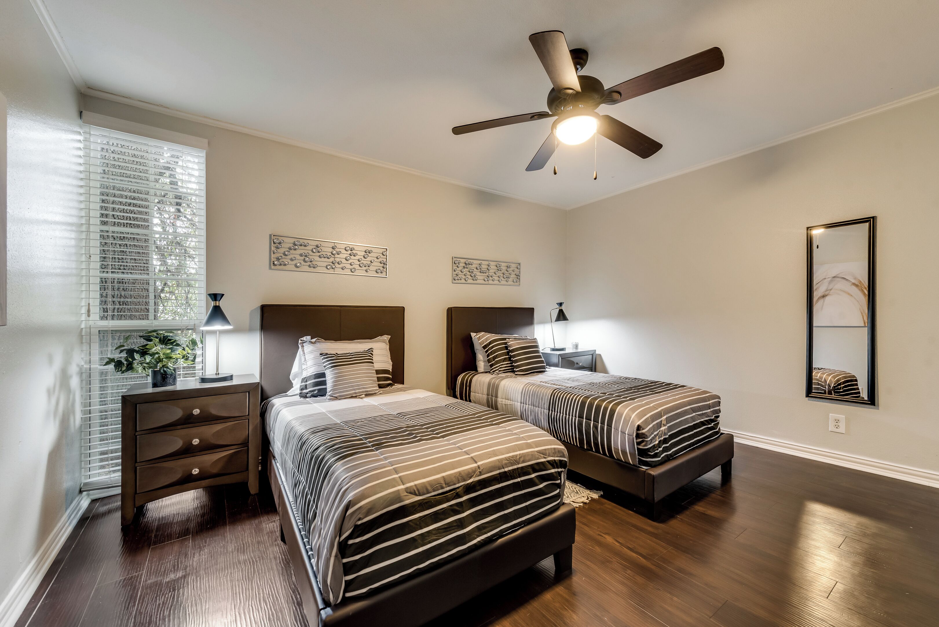 Une chambre avec deux lits, un ventilateur de plafond et une fenêtre avec des stores.