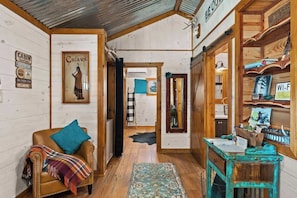 Interior de una cabaña con un sillón de cuero, una mesita, paredes de madera y un techo de metal.