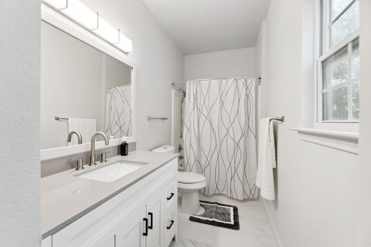 A modern bathroom with a white vanity, a toilet, and a shower with a patterned curtain.