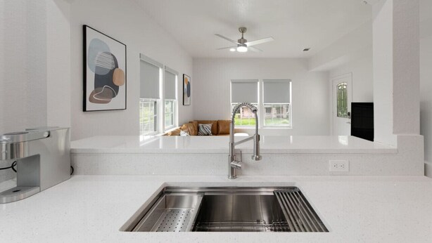 Eine moderne Küche mit Spüle aus Edelstahl, Deckenventilator und großen Fenstern mit Blick ins Freie.