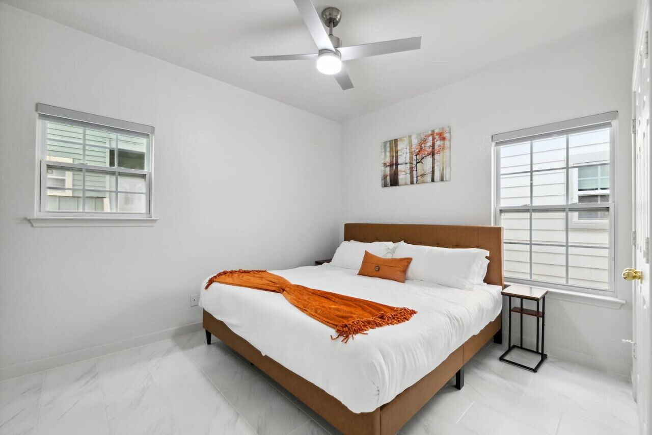 A bedroom with a bed, white walls, a ceiling fan, and two windows.