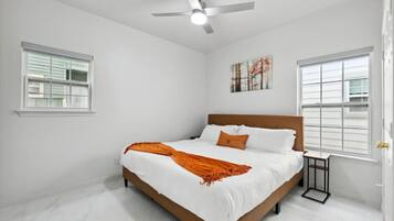 A bedroom with a bed, white walls, a ceiling fan, and two windows.