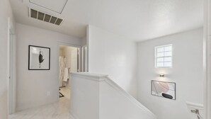 Ein Flur mit weißen Wänden, einem gerahmten Bild, einem kleinen Fenster und einer Treppe.