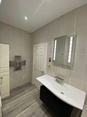 A modern bathroom with a white sink, a glass shower enclosure, and a door with a mirror above it. - Immaculate 1-bed Lux Apartment in Wolverhampton (Wolverhampton)
