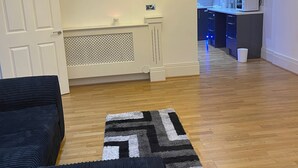A living room with a dark sofa, a patterned rug, and a kitchen in the background. - Immaculate 1-bed Lux Apartment in Wolverhampton (Wolverhampton)