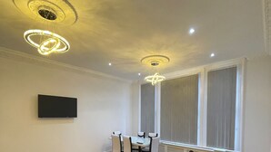 A modern living room with a black sofa, a dining table with chairs, a TV mounted on the wall, and a ceiling with recessed lighting and decorative elements. - Immaculate 1-bed Lux Apartment in Wolverhampton (Wolverhampton)
