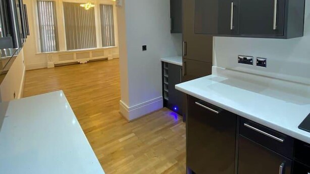 A modern kitchen with dark cabinets, a white countertop, and blue under-cabinet lighting. - Immaculate 1-bed Lux Apartment in Wolverhampton (Wolverhampton)