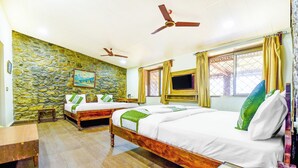 Een hotelkamer met twee eenpersoonsbedden, een stenen muur, een houten vloer, een flatscreen televisie en plafondventilatoren.