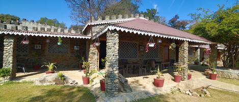 A stone building with a tiled roof, outdoor seating, and potted plants.