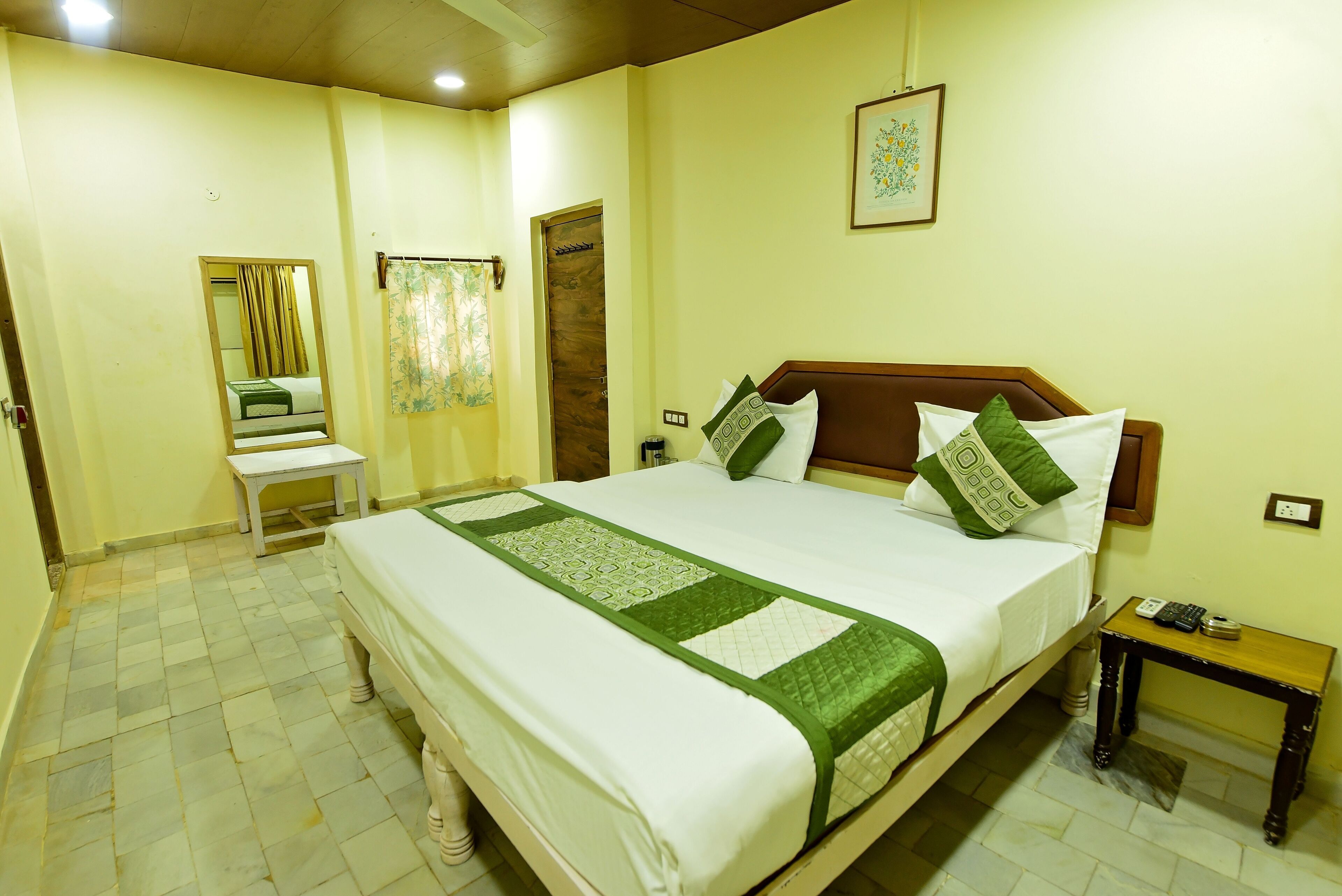 A neatly arranged hotel room with a large bed, a small table, a chair, and a mirror.