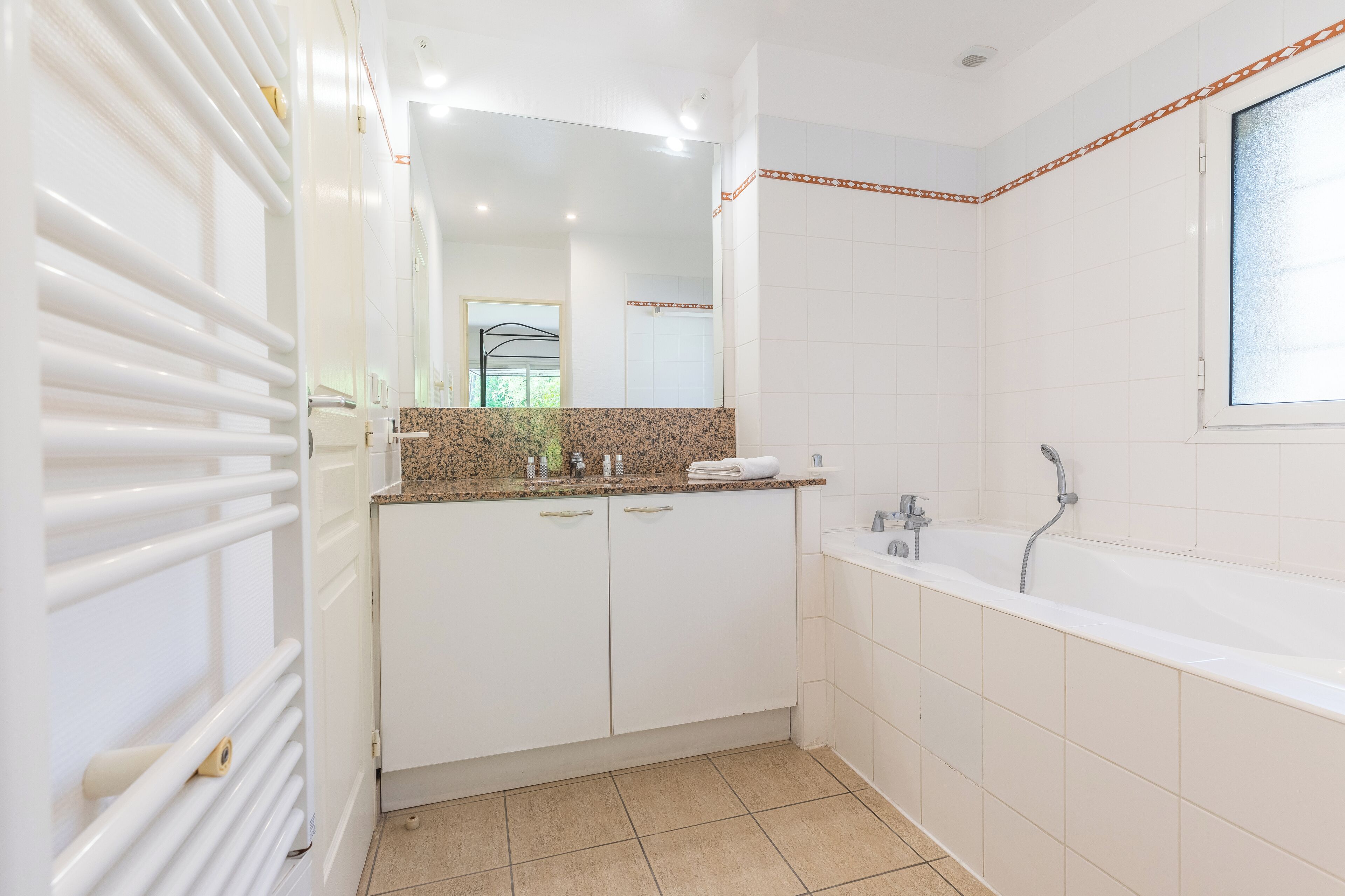 A modern bathroom with a large bathtub, white cabinetry, and a mirror above the sink.