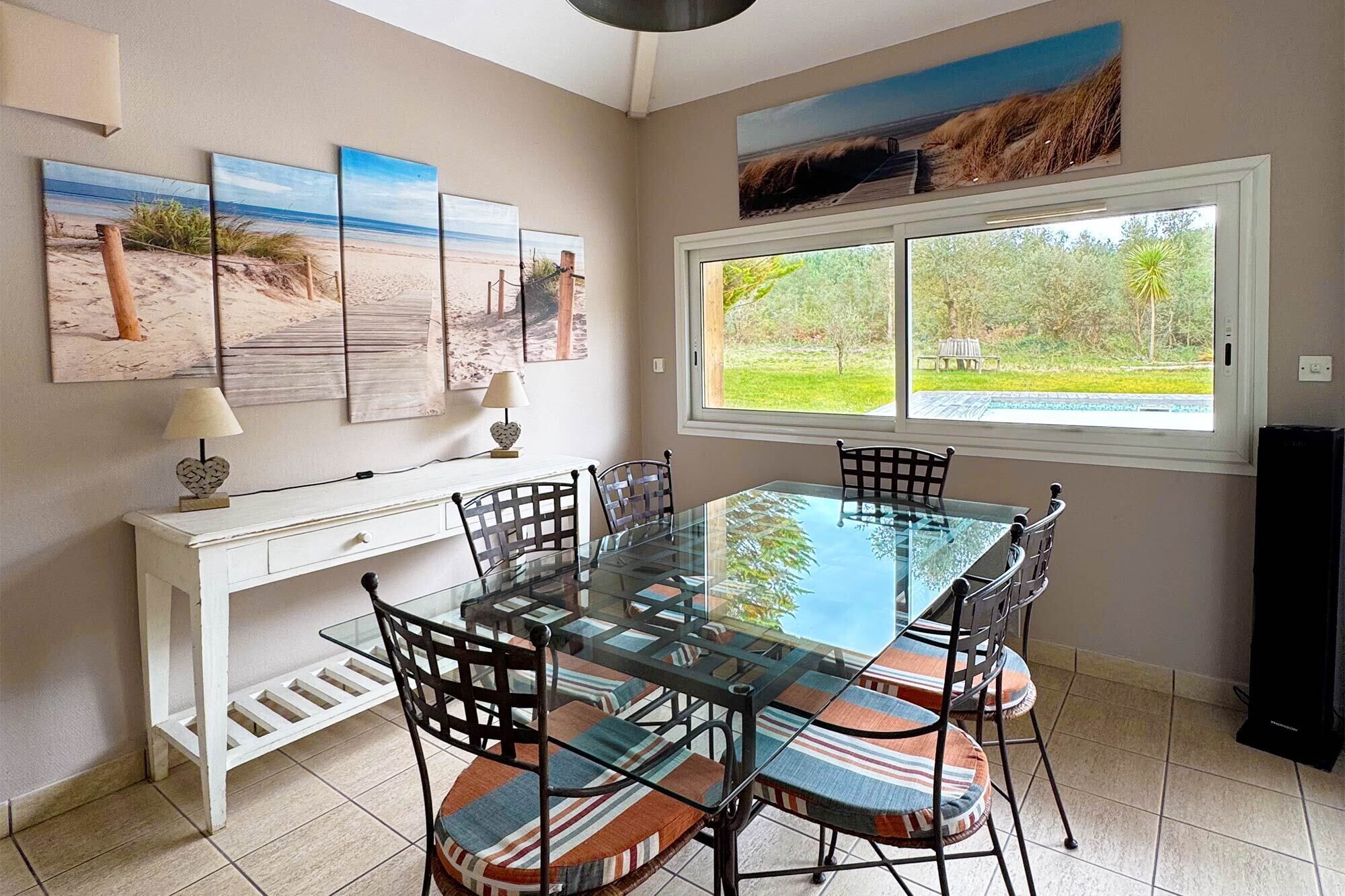 A dining area with a glass table, six chairs, a white console table, and artwork on the wall.