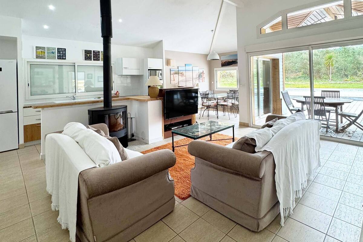 A modern living room with a fireplace, sofa, TV, and dining area with outdoor view.