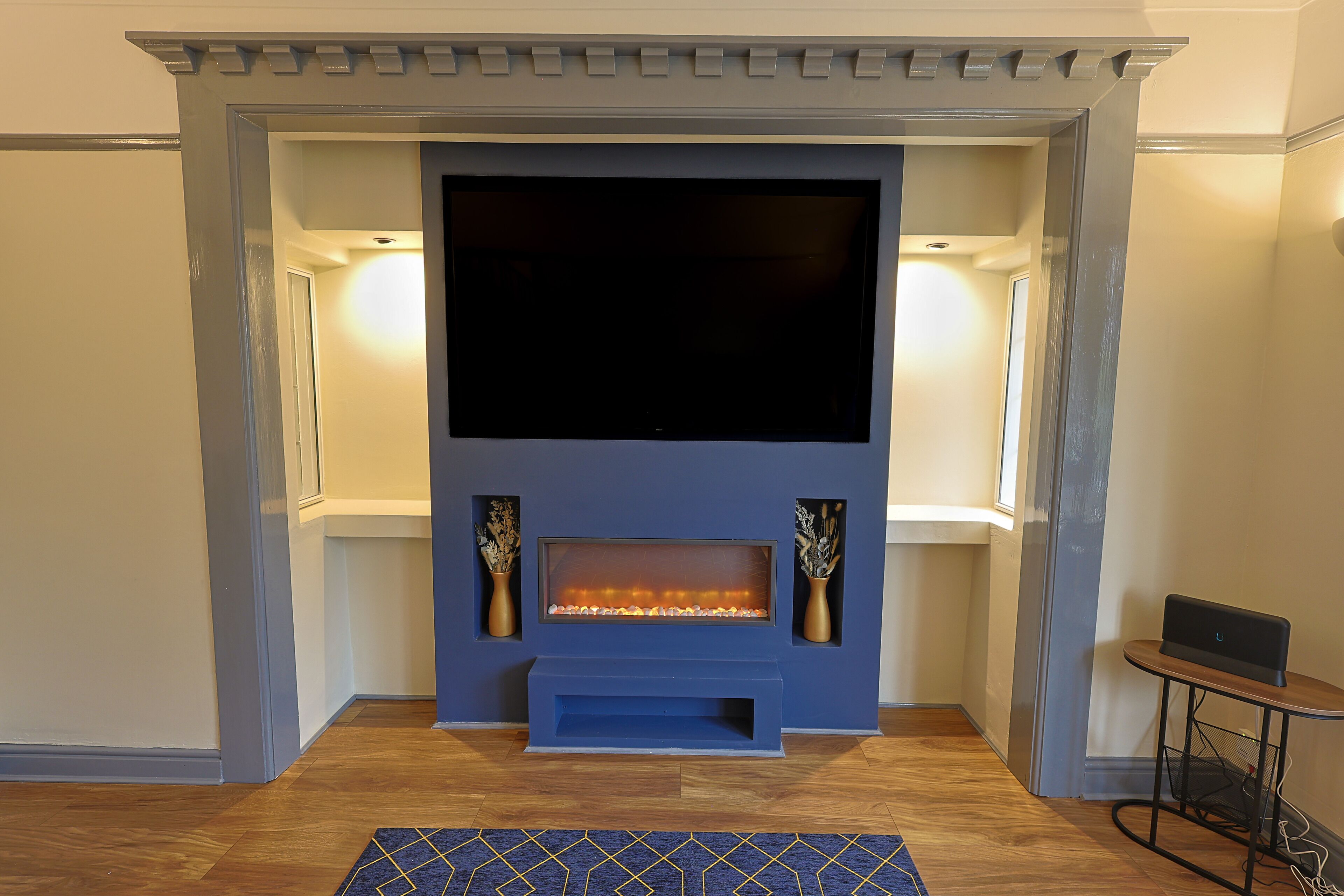A modern living room with a large flat-screen TV, a fireplace, and a small side table.