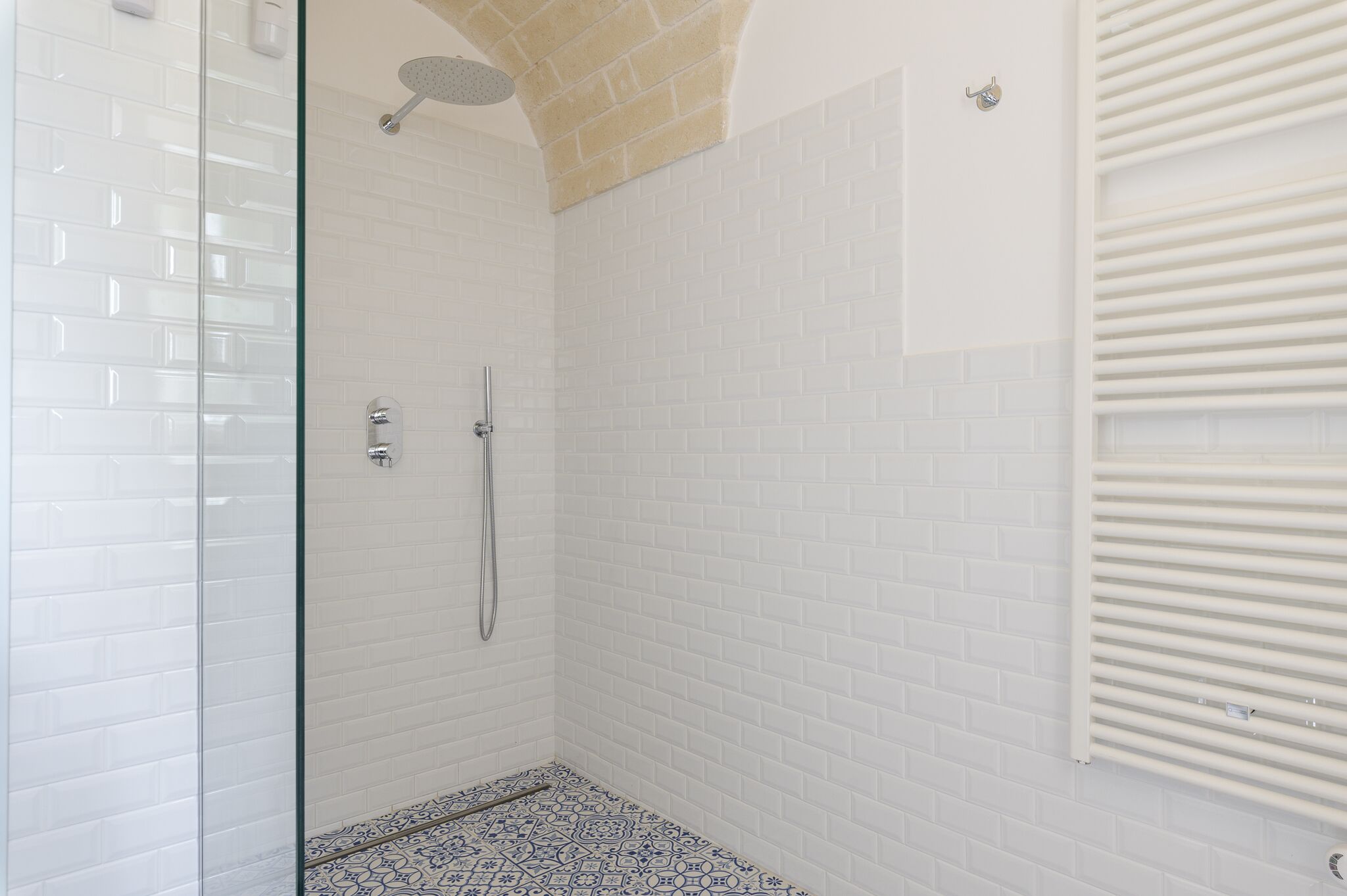 Een douche met witte betegelde wanden en een glazen deur, een douchekop en een handdouche.