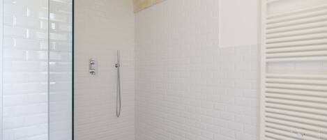 Een douche met witte betegelde wanden en een glazen deur, een douchekop en een handdouche.