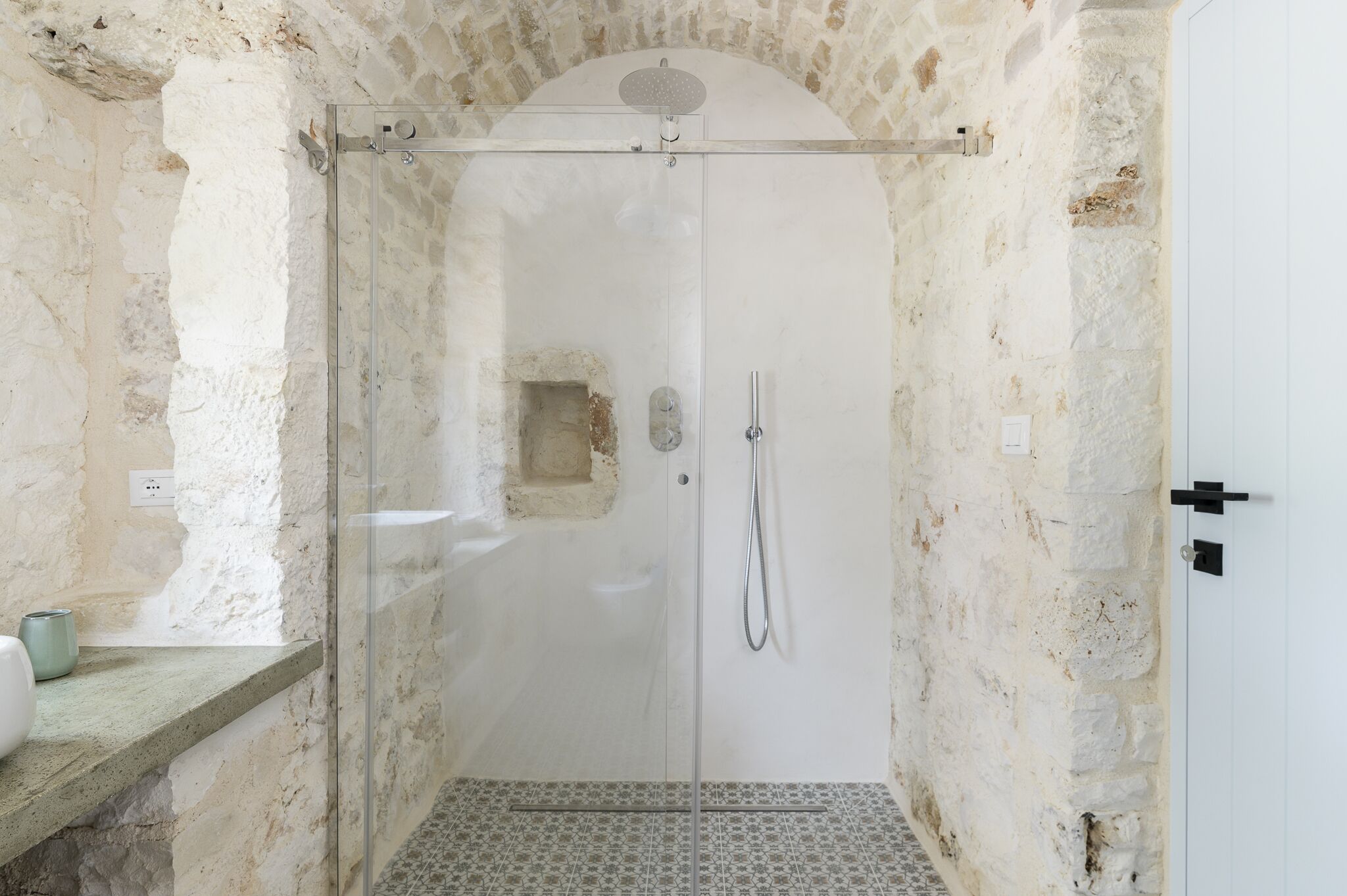 A shower with a glass door, stone walls, and a small window.