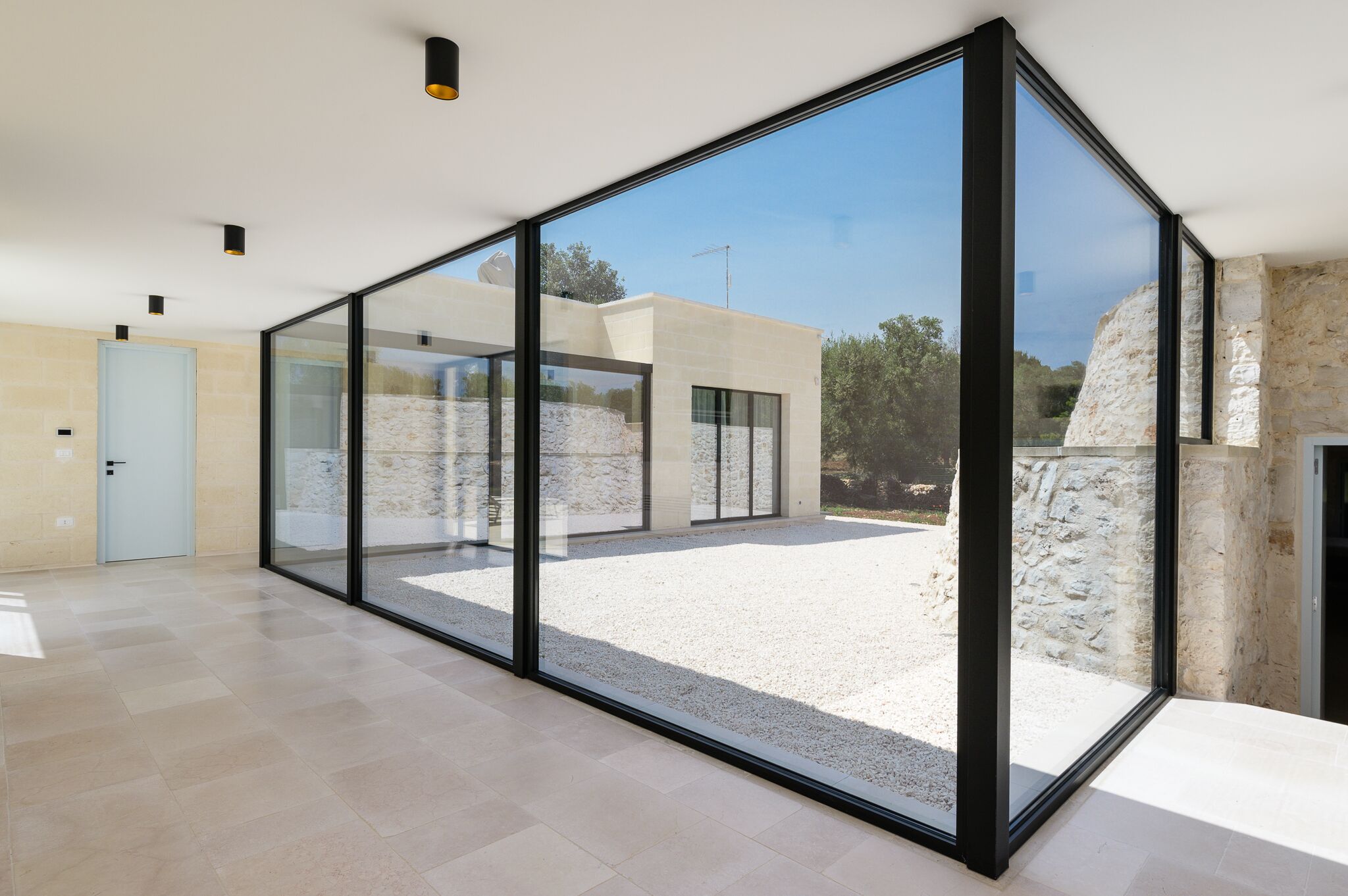 A modern interior with large glass doors leading to an outdoor area, a light-colored tiled floor, and a stone wall.