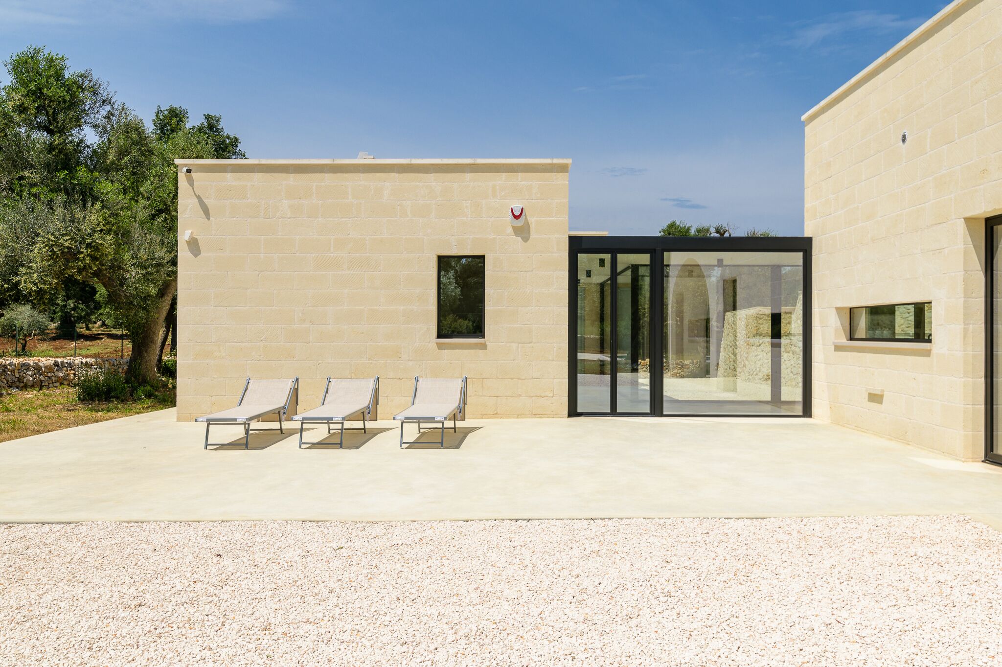 A building with a beige brick exterior, a glass door entrance, and three lounge chairs in front.