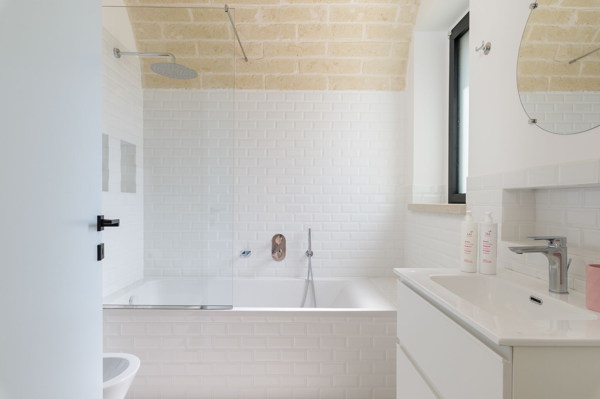 A modern bathroom with a white-tiled shower, a bathtub, and a vanity with a mirror and sink.