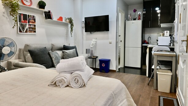 Een moderne hotelkamer met een bed, een televisie, een kitchenette en een ventilator.