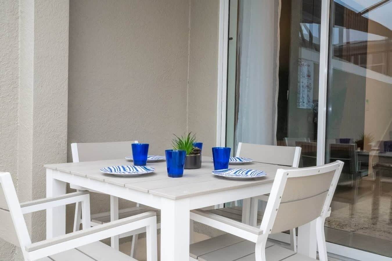 Een witte tafel met blauwe borden en glazen, een potplant en een glazen deur naar een buitengebied.