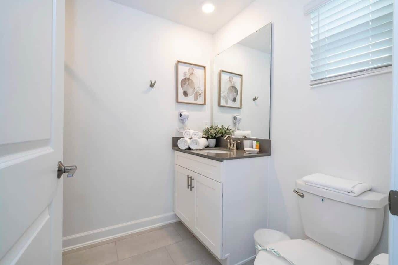 A modern bathroom with a toilet, sink, and mirror. There are towels and toiletries on the sink counter.