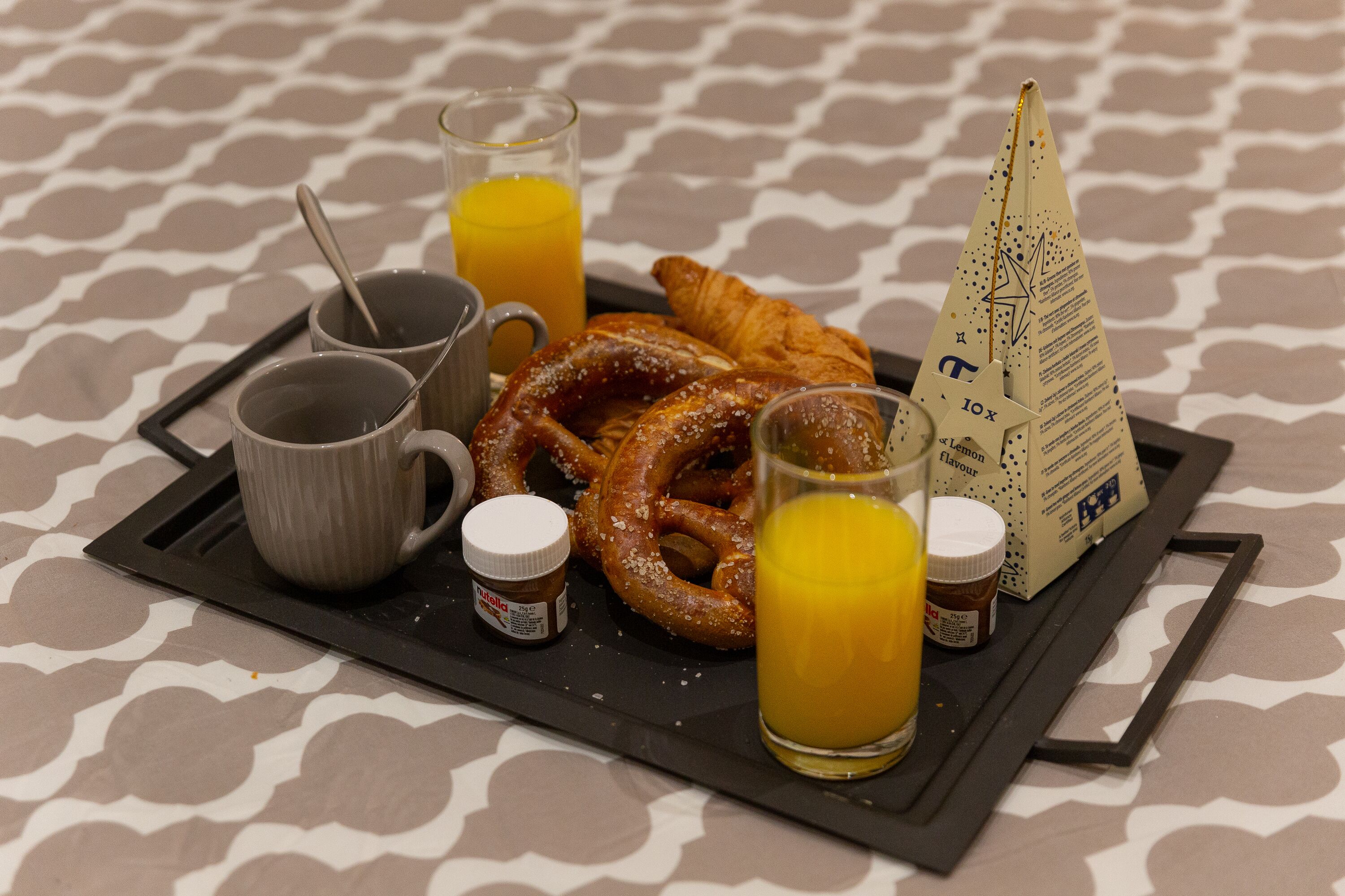 Un plateau contenant des articles pour le petit-déjeuner, notamment des croissants, des bretzels et du jus, ainsi que des condiments et un porte-serviettes.