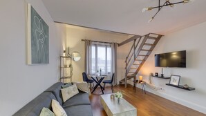 A modern living room with a gray sofa, a coffee table, a TV, and a staircase. - Charmant Duplex 30 min Paris (Corbeil-Essonnes)