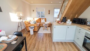 Ein modernes Wohnzimmer mit Sofa, Esstisch gedeckt mit Tellern und Gläsern, Küchenzeile mit Mikrowelle und Schränken sowie Treppe zu einer weiteren Ebene.