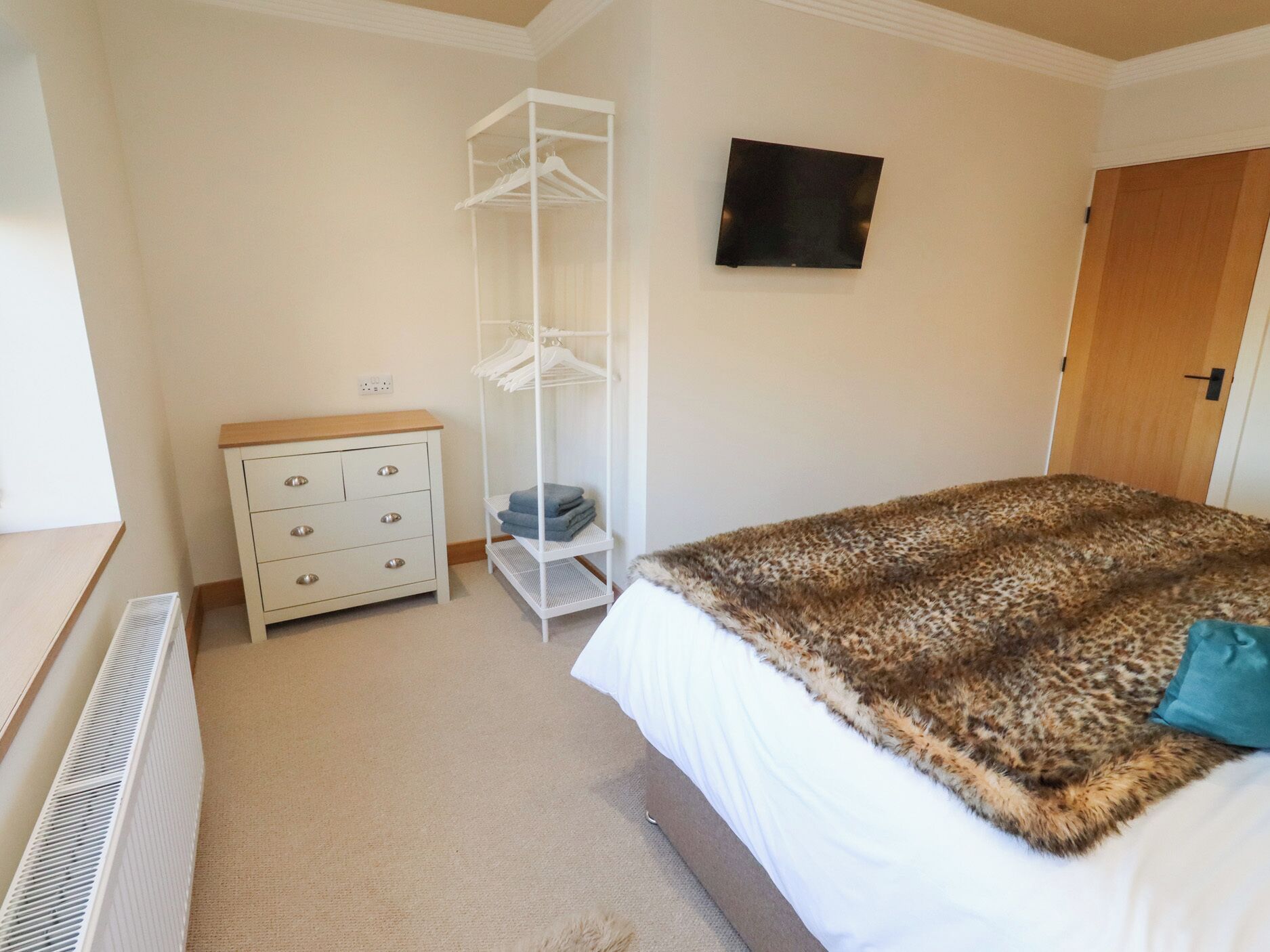 A bedroom with a bed, a dresser, a radiator, a wardrobe, and a TV on the wall.