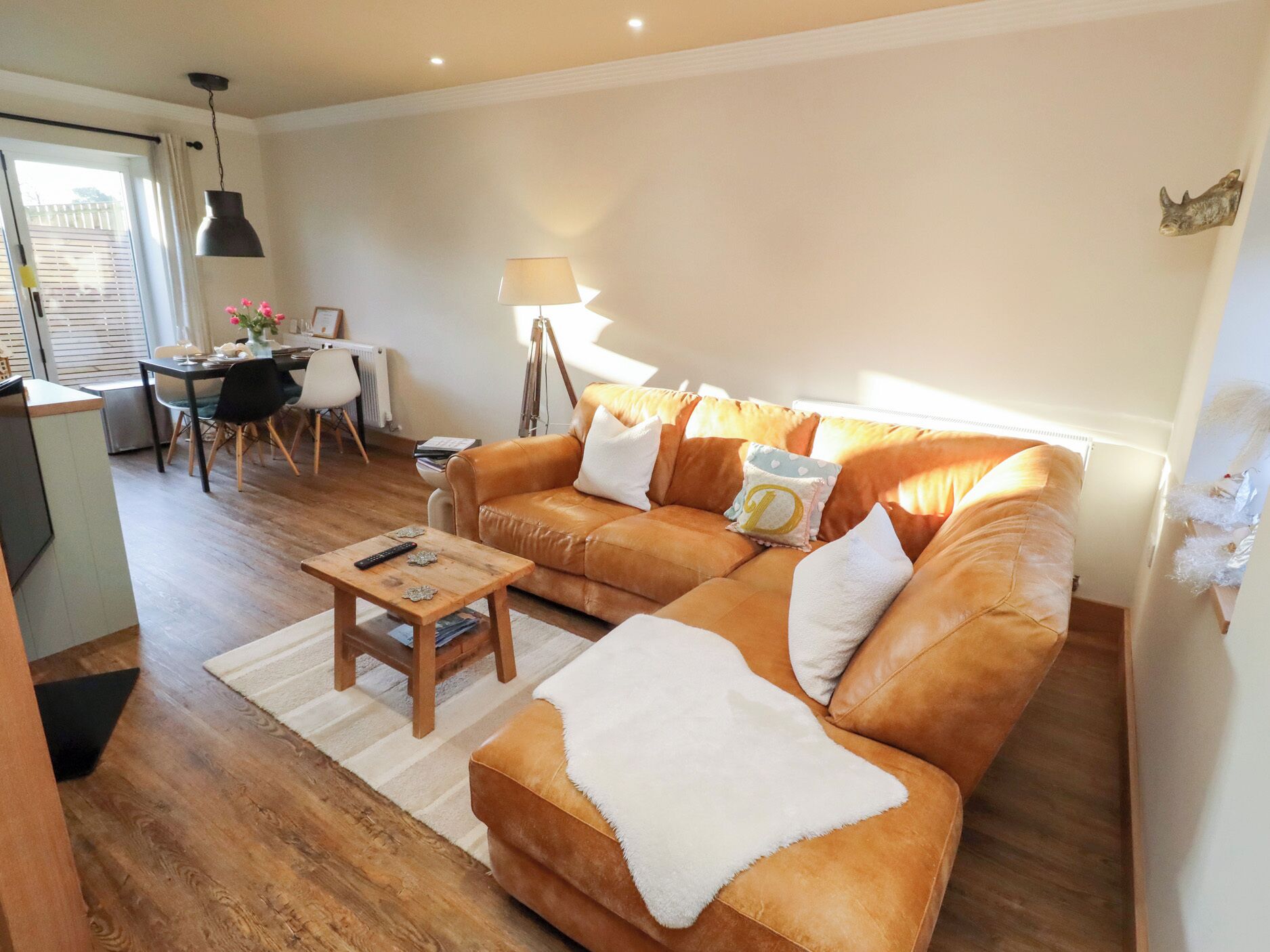 A cozy living room with a brown leather sofa, a wooden coffee table, and a dining area with a table and chairs.
